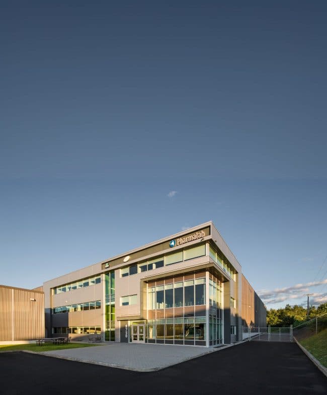 Un bâtiment PharmaLab moderne de deux étages avec de grandes fenêtres et une aire pavée devant.