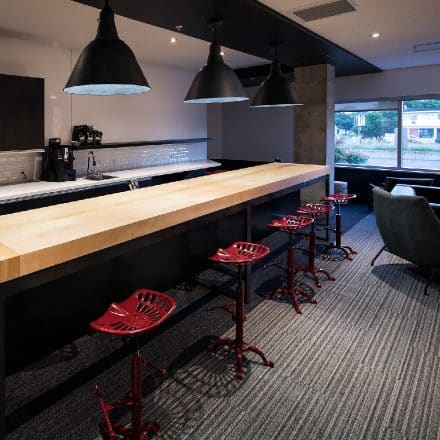 Un long comptoir en bois avec des tabourets rouges en forme de siège de tracteur et des lampes suspendues noires.