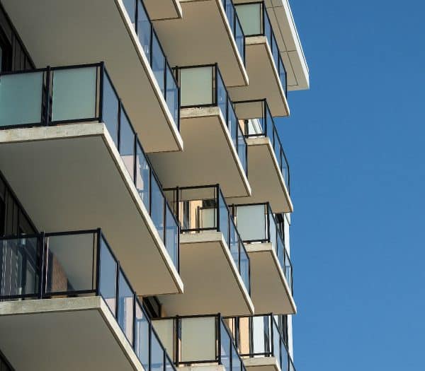 Vue rapprochée des balcons d'un immeuble moderne avec des balustrades noires sur un ciel bleu clair.