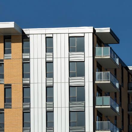 Un immeuble d'appartements moderne avec un mélange de briques et de bardage métallique, comprenant plusieurs balcons.