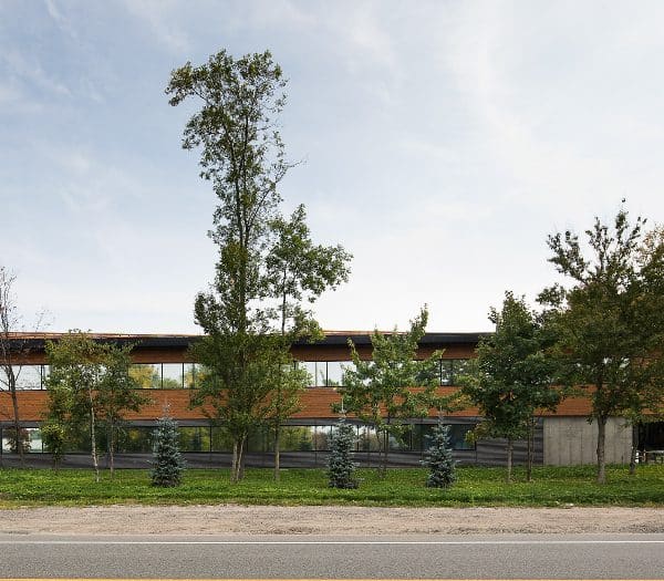 Un bâtiment moderne avec de grandes fenêtres est situé derrière une rangée d'arbres.
