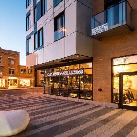 Vue de rue d'un Starbucks au crépuscule, à côté d'un immeuble moderne.