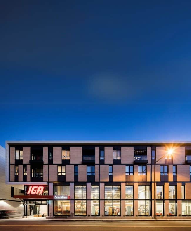 Une épicerie IGA la nuit, située dans un immeuble moderne en brique.