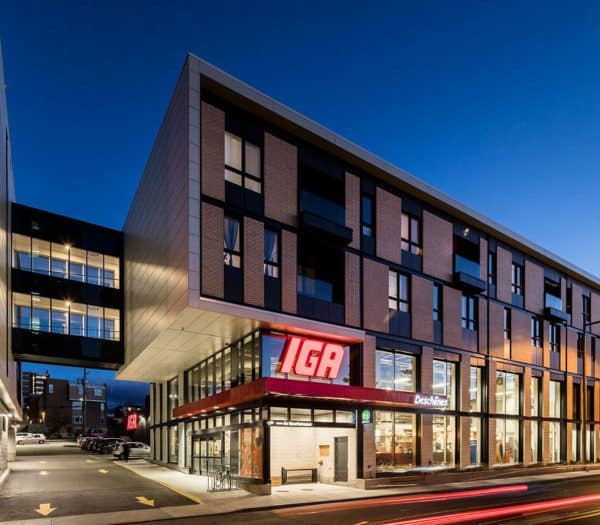 Vue nocturne d'un immeuble moderne avec un supermarché IGA au rez-de-chaussée.