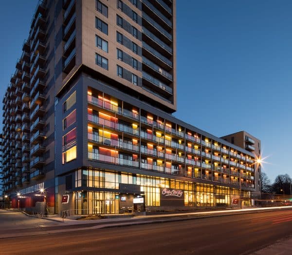 Un immeuble d'appartements moderne avec des balcons illuminés et un espace commercial au rez-de-chaussée au crépuscule.